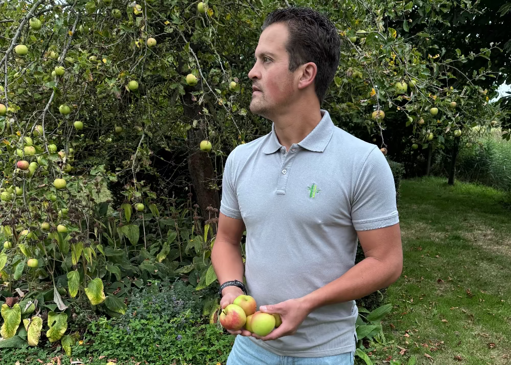 Man in the garden with apples in his hands waring a gey bamboo polo